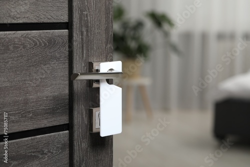 Wooden door with blank hanger on metal handle, closeup photo