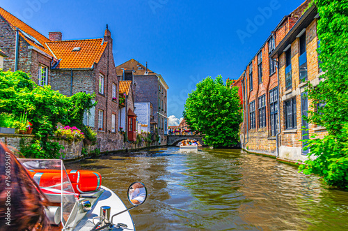 Bakkersrei water canal with tourists boat, Mariabrug bridge and medieval buildings walls with green plants in Brugge old town district, Bruges city historical center, West Flanders province, Belgium photo