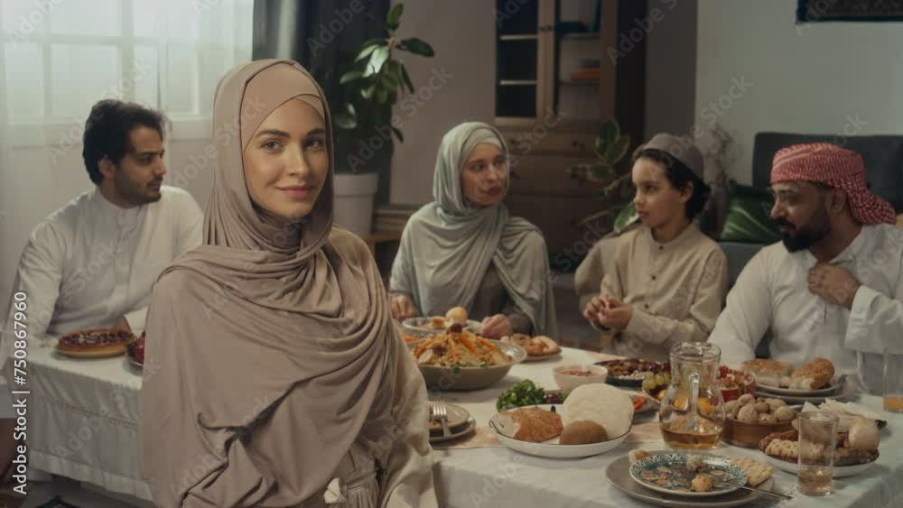 Slowmo portrait of young pretty covered lady wearing hijab and abaya posing by festive table on Eid al-Fitr celebration day at home with relatives Slowmo portrait of young pretty covered lady wearing hijab and abaya posing by festive table on Eid al-Fitr celebration day at home with relatives