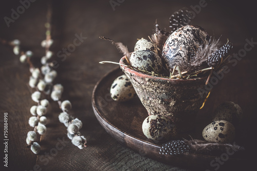 Easter decoration: rustic flower pot with natural quail eggs and feathers on a dark wooden plate and table