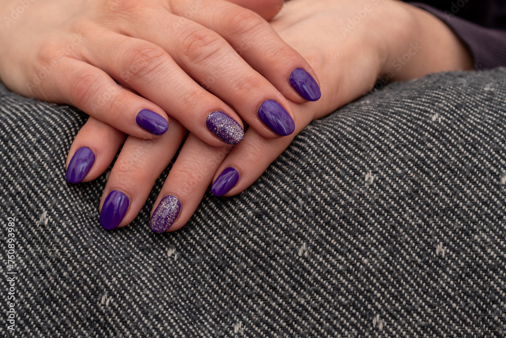 Fototapeta premium Well-groomed woman's hands resting on a uniform gray towel. Purple glitter nail polish with freshly applied. Brilliant trilogy diamond ring. Beautiful manicured hands. Selective focus and Copy space.
