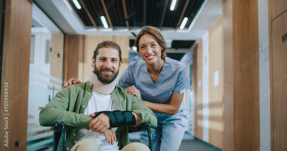 Obraz premium Portrait of happy injured Caucasian man recovering in hospital with qualified female doctor looking at camera and smiling. Bearded young patient and helpful nurse in modern clinic.