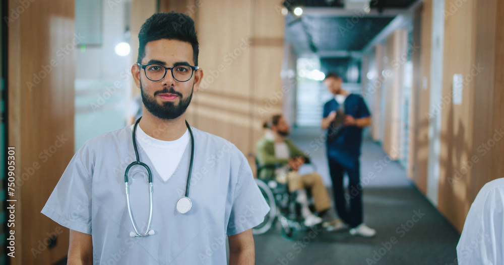Portrait of happy professional qualified doctor standing in corridor of cozy hospital holding stethoscope and glasses looking at camera and smiling. Patient in wheelchair on background. Portrait of happy professional qualified doctor standing in corridor of cozy hospital holding stethoscope and glasses looking at camera and smiling. Patient in wheelchair on background.