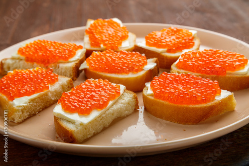 Canapes with red caviar on a plate on a wooden table. Horizontal