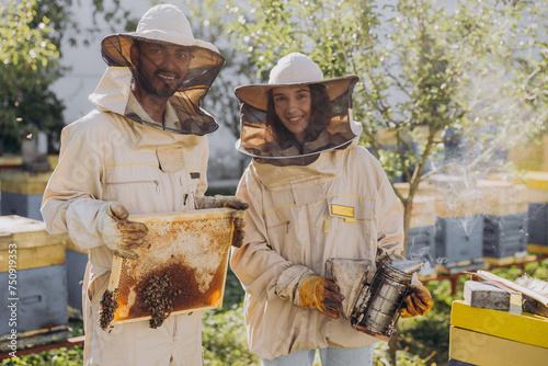 Couple of happy smiling beekeepers working with beekeeping tools near beehive at bee farm © anatoliycherkas