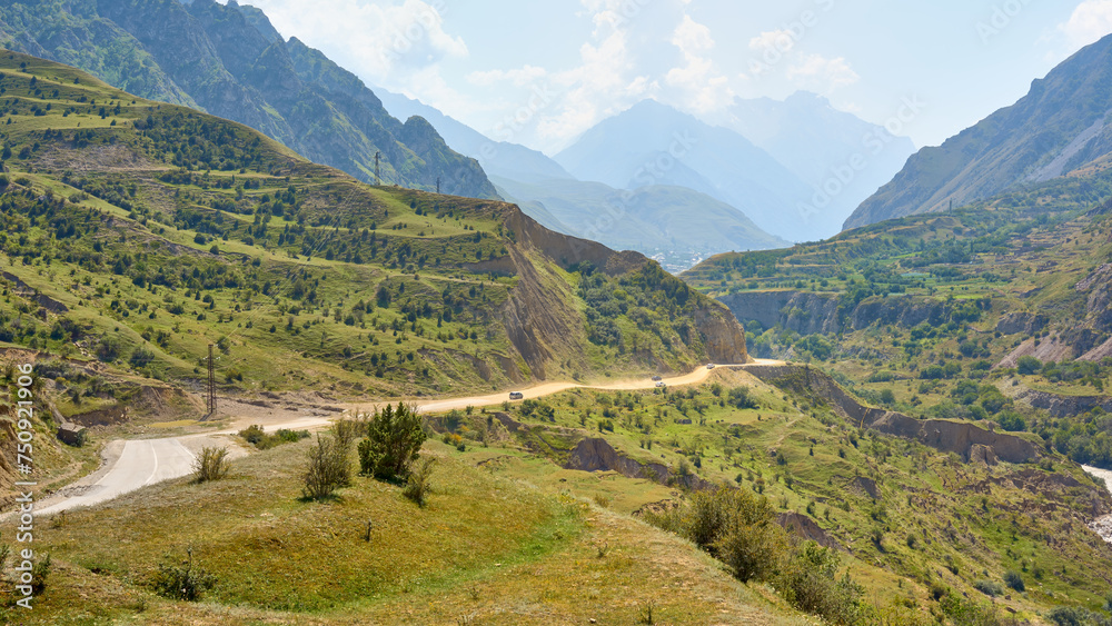 Beautiful mountain road to the village of Upper Balkaria. Cars move along a dusty winding mountain road on a bright summer day.
