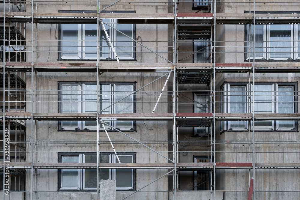 Facade wall on a construction site in Europe, Scaffolding among windows. Unfinished modern apartment architecture building site.