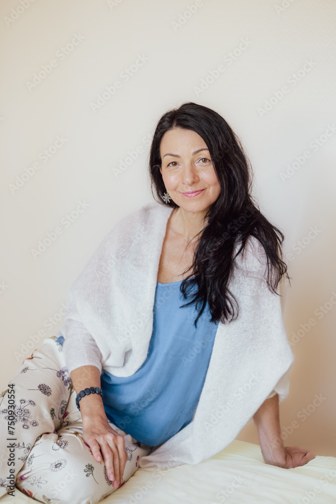 Smiling woman with black hair, blue top, white shawl, sitting comfortably. Her relaxed posture and warm expression evoke a sense of homey contentment. Smiling woman with black hair, blue top, white shawl, sitting comfortably. Her relaxed posture and warm expression evoke a sense of homey contentment.