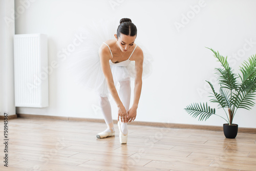 Beautiful graceful ballerina in black swan dress. Young ballet dancer practicing before performance in black tutu, classical dance studio, stretching her back touching feet with hands, copy space.