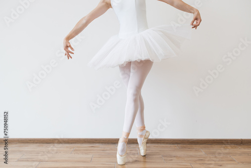 Close up of legs of Caucasian ballerina in white bodysuit and tutu poses in motion showing ballet elements while standing on pointe shoes.
