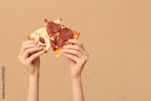 Female hands holding tasty pizza slices on beige background