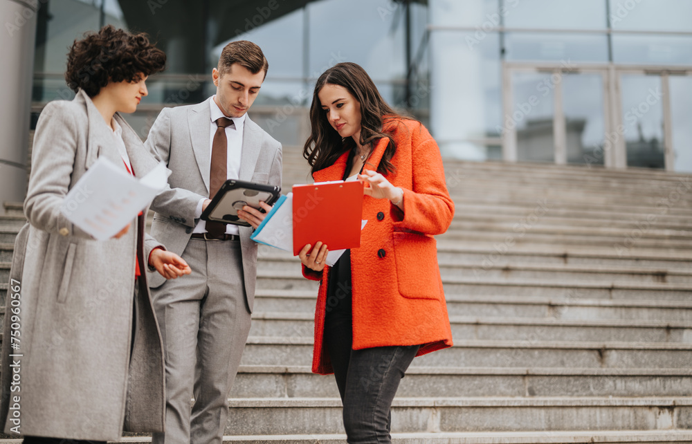 Fototapeta premium Three business colleagues engaging in a discussion with documents and digital tablet on the steps outside their office building.