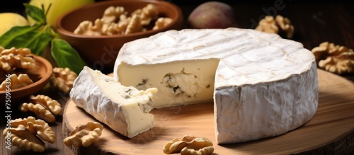 A piece of black cheese and white camembert with a white crust is surrounded by walnuts on a wooden board.