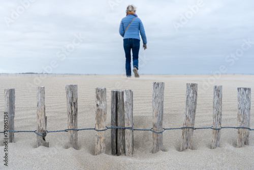 une barrière en bois ensevelie dans le sable avec une femme de dos en fond