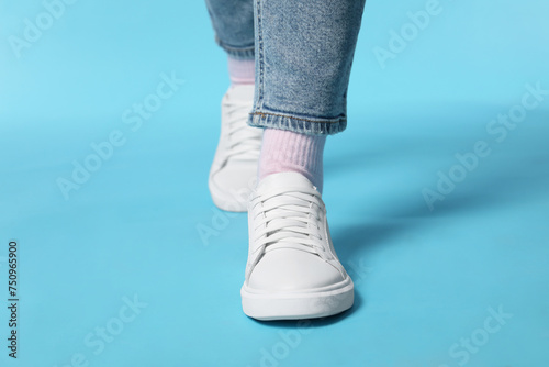 Woman wearing stylish white sneakers on light blue background, closeup