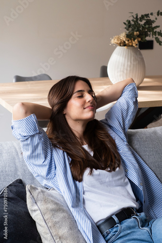 Portrait of a girl relaxing on a sofa after work at home sitting on a sofa in the living room at home. One young woman stretching arms and rest in indoor leisure activity relaxing on couch. People