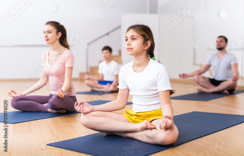 Tween girl exercising with brother, mother and father at yoga class, concept of healthy family lifestyle