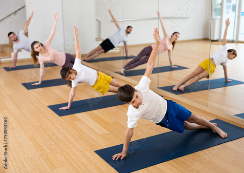 Fit woman, man and teenage girl and boy performing yoga exercises on gymnastic mats at yoga studio, physical, emotional and spiritual family health concept