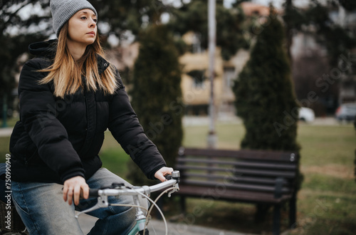 Casual woman riding a bicycle in an urban park during winter season.