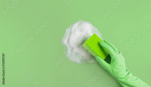 Hand in green rubber glove holding washing sponge