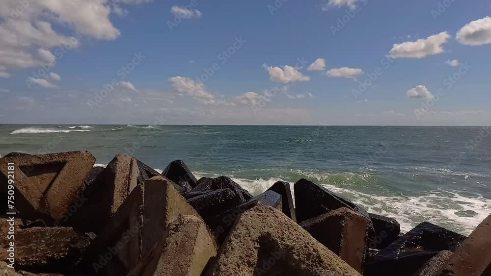 Waves crashing against stone breakwater near shore. Wave splash on pier in sea. Fresh wind on sea, choppy sea with long waves and whitecaps. Outdoor Seascape on sunny summer day. Waves crashing against stone breakwater near shore. Wave splash on pier in sea. Fresh wind on sea, choppy sea with long waves and whitecaps. Outdoor Seascape on sunny summer day.