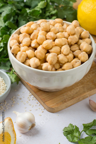Chickpeas in a bowl, lemon, olive oil, sesame, cilantro, garlic on a wooden board, on a light background. The process of making hummus. Eastern cuisine.
