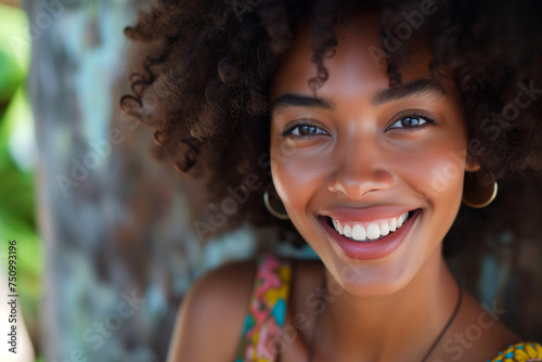 Close-up portrait of a joyful African American woman with curly hair and a bright smile, natural backdrop. © Sascha