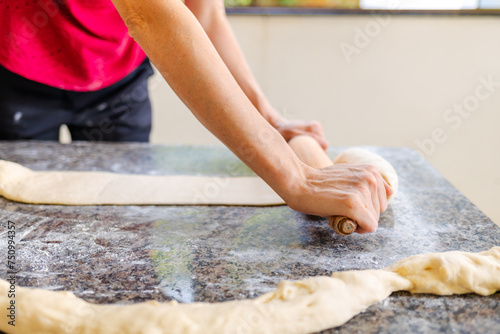 Rolling out bread dough with a rolling pin on the table. Next to her, there is raw stretched dough waiting to be worked. Making homemade bread at home