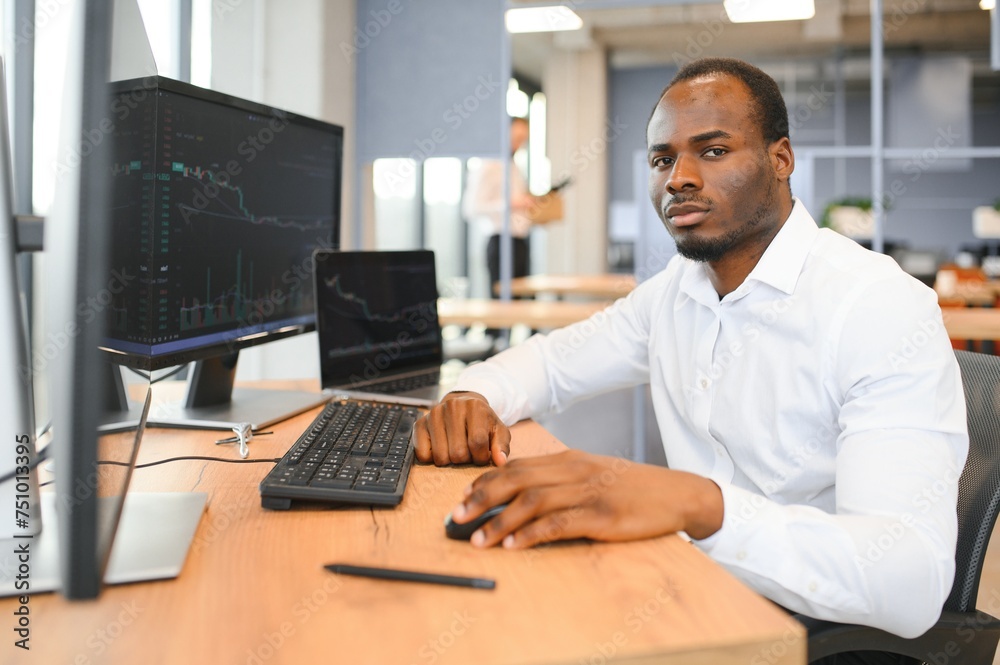 African American trader works at computer with displayed real-time stocks