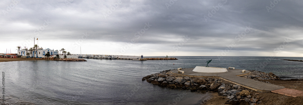 Panoramic photograph of the circular breakwater on the beach of El Faro de Marbella and the fountain with La Venus, the lady of Marbella. Stormy sky. Marbella, Spain