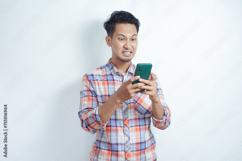 Adult Asian man showing rage expression when looking to his cellular phone Adult Asian man showing rage expression when looking to his cellular phone