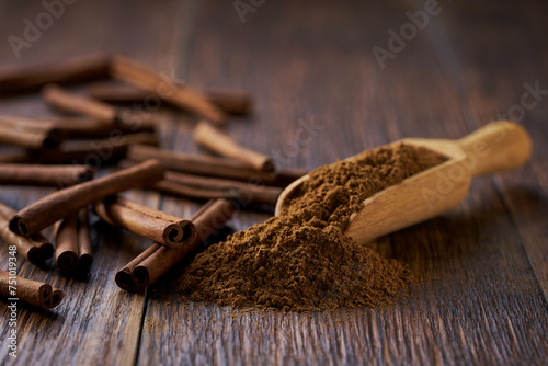 cinnamon powder poured out of a wooden spoon on a dark wooden table, selective focus.