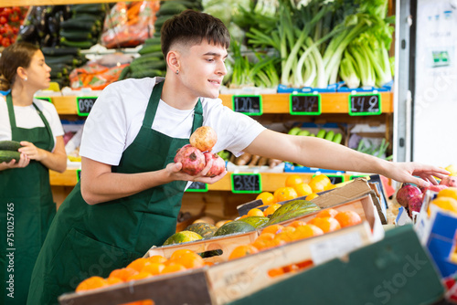 Hardworking young salesman working in a vegetable store puts pomegranates on the counter