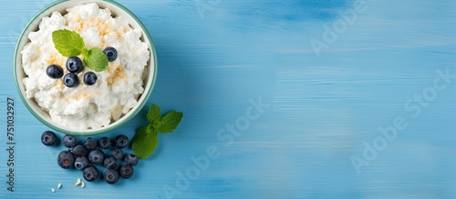 A bowl filled with creamy yogurt topped with plump blueberries and fresh mint leaves on a turquoise background. The vibrant colors and textures create a visually appealing and nutritious breakfast