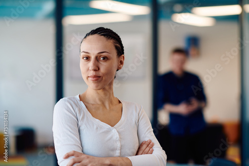 Portrait of a business woman in a creative open space coworking startup office with crossed arms. Successful businesswoman standing in office with copyspace. Associates work in the background © .shock