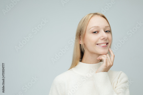 young woman dressed casual touches her face over grey background