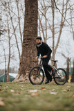 A young, bearded man rides a mountain bike outdoors with determination, amid fallen leaves on an autumn day. A sense of adventure and fitness lifestyle is captured.