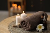 Spa composition. Rolled towel, cosmetic products, stones, burning candles and plumeria flower on table indoors, closeup