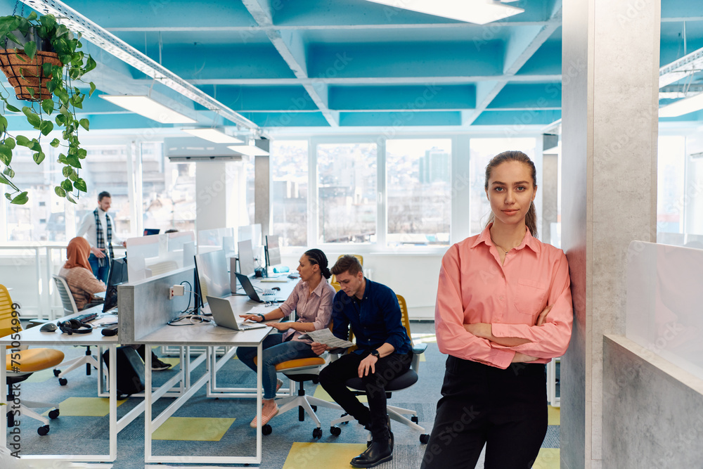 Portrait of young smiling business woman in creative open space coworking startup office. Successful businesswoman standing in office with copyspace. Coworkers working in background Portrait of young smiling business woman in creative open space coworking startup office. Successful businesswoman standing in office with copyspace. Coworkers working in background