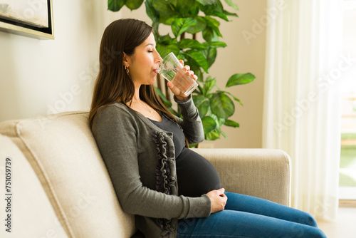 Beautiful pregnant woman drinking water and relaxing on the couch