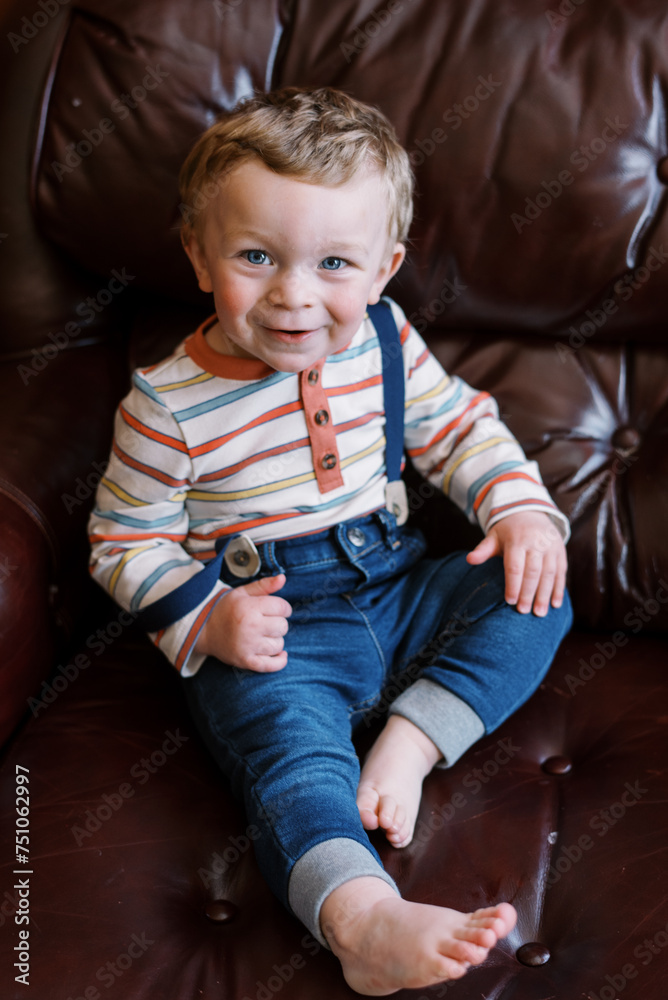 cute little boy smiling while sitting on couch at home cute little boy smiling while sitting on couch at home