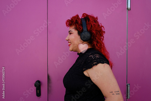 queer person over pink background listening to music on headphones photo