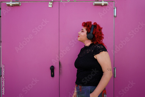 queer person over pink background listening to music on headphones photo
