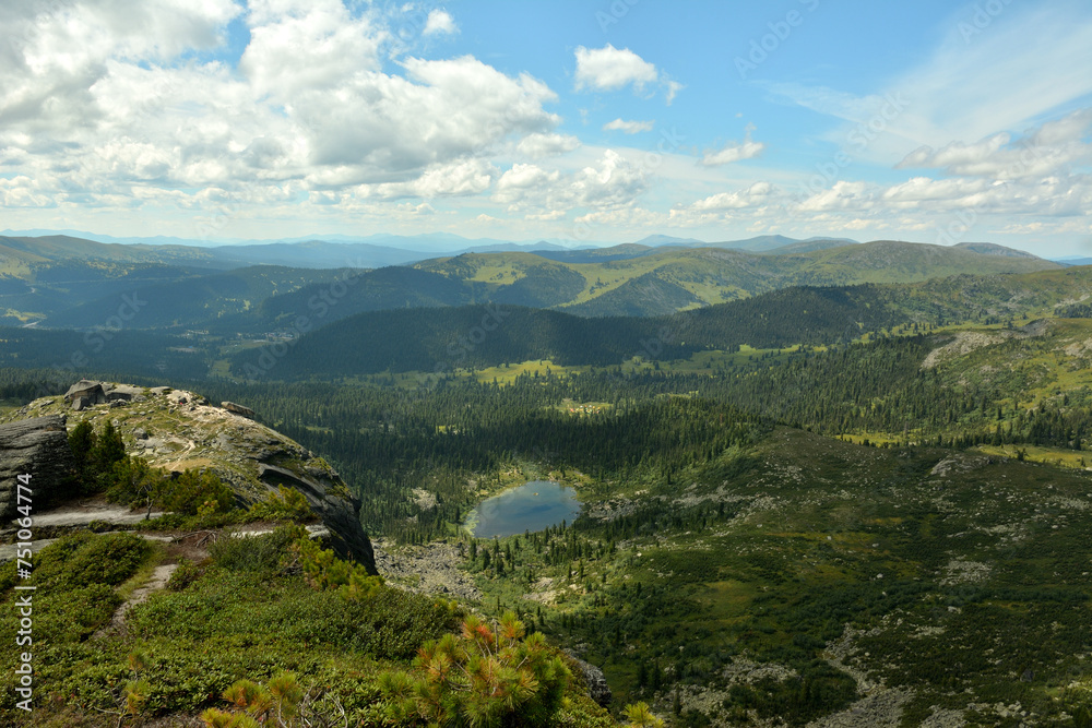 View from the top of the mountain to the dense taiga on the ridges and a small picturesque lake in the lowland.