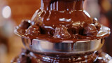 Small bitesized treats being dipped into a chocolate fountain their surfaces perfectly coated in a thick layer of creamy chocolate.