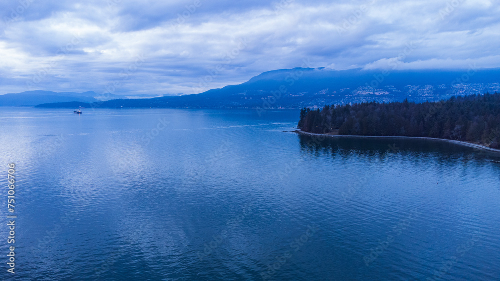 Edge of Stanley Park with West Vancouver and mountains in the background at sundown on a cloudy evening
