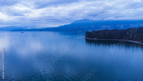 Edge of Stanley Park with West Vancouver and mountains in the background at sundown on a cloudy evening