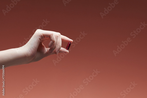 woman hand holding yellow pill capsule on red background photo