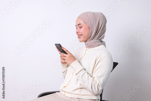 Side view of young muslim woman using smartphone while sitting on chair 
