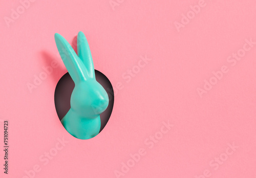 Creative composition with blue Easter bunny rabbit peeking out from hole on pink  background. Creative art, Contemporary style. Minimal easter concept, with writing space and copy space